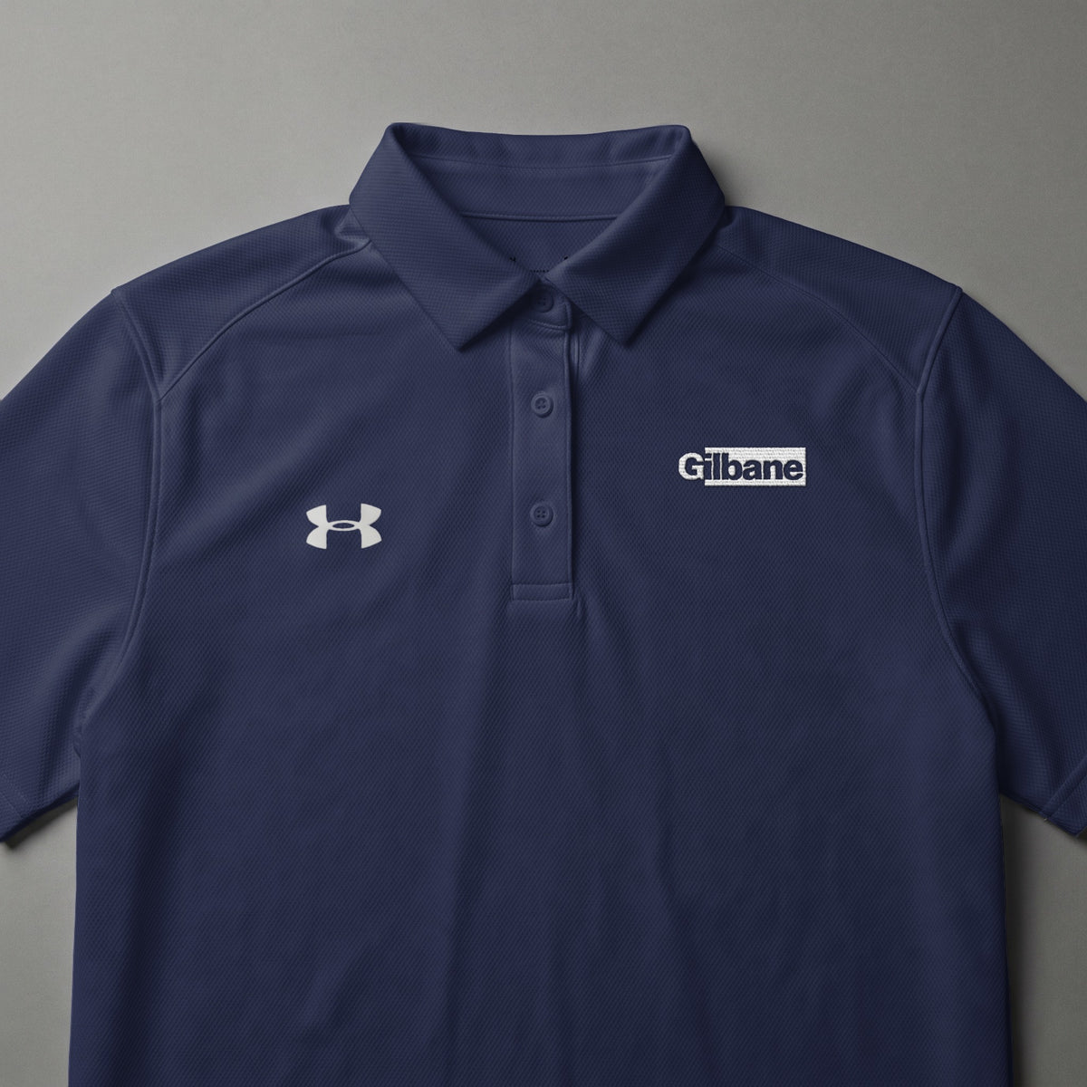 Navy Under Armour polo shirt with Gilbane logo on chest.
