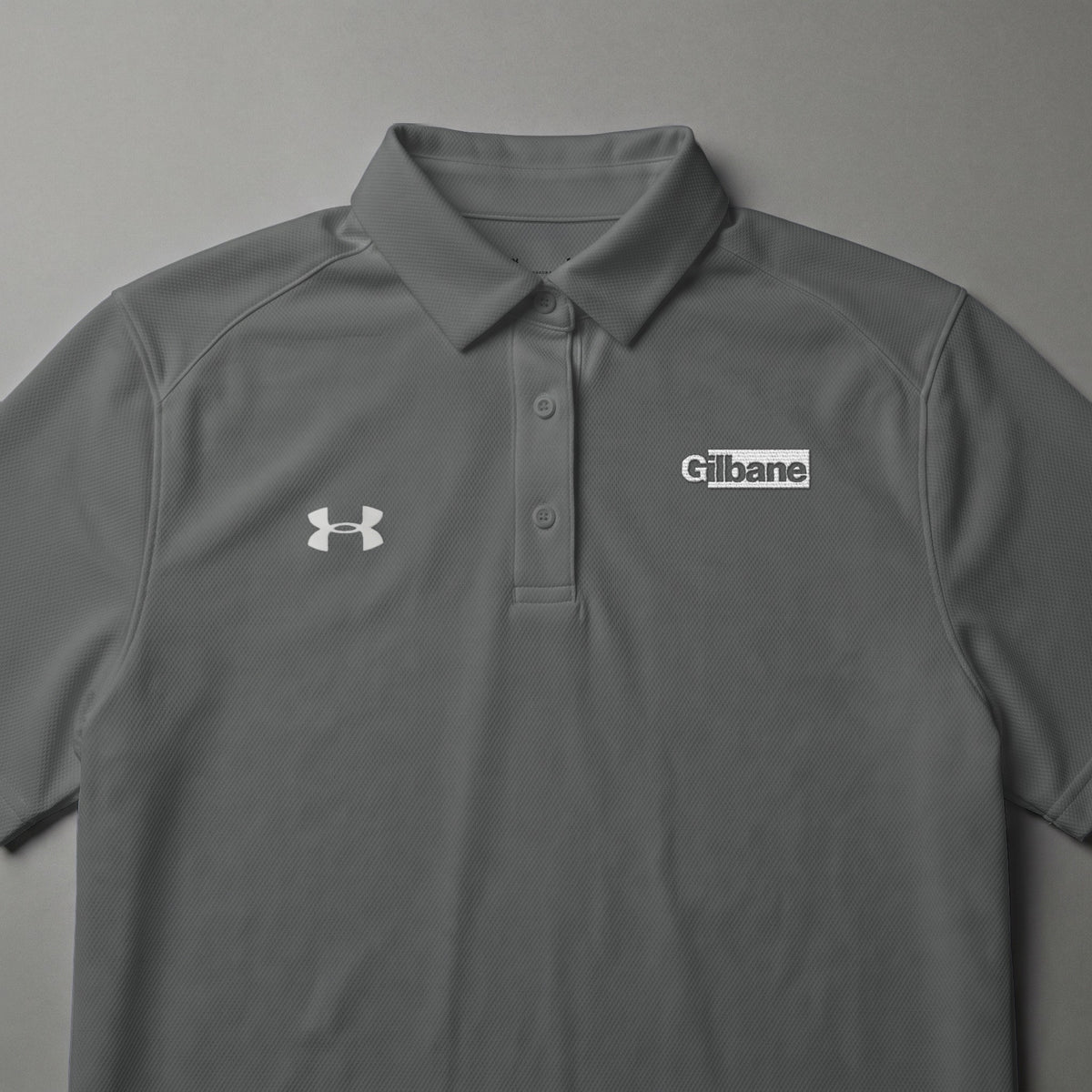 Gray Under Armour polo shirt with Gilbane logo on chest.