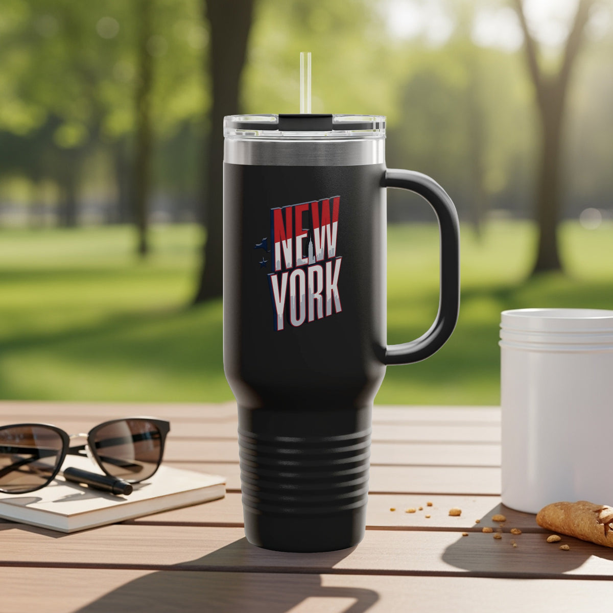 Black travel mug with "NEW YORK" text and graphic, outdoors.