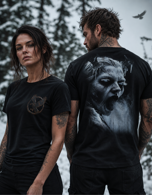 Two models wearing black graphic t-shirts in an outdoor snowy setting. The woman on the left shows the front of her black t-shirt which features a small metallic gold Mockingbird logo on the left chest.