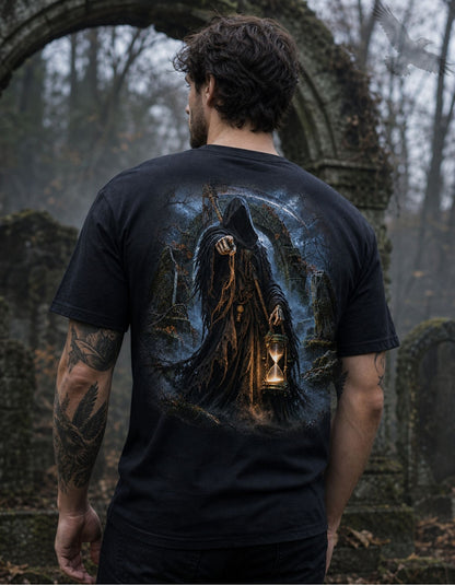 A man viewed from behind wearing a black graphic t-shirt with a detailed illustration of a hooded figure holding a glowing hourglass in a graveyard setting. The background is a blurred, misty forest cemetery.