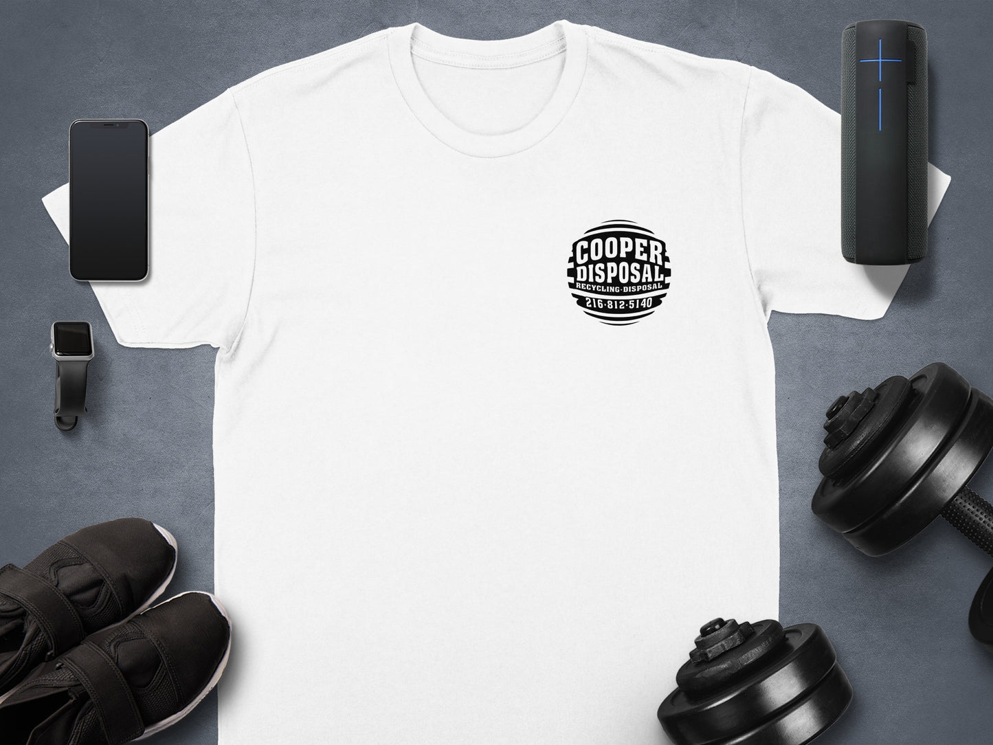 White t-shirt with Cooper Disposal logo, black dumbbells, and smartphone on gray background.