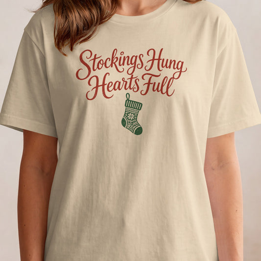 Cream t-shirt with "Stockings Hung Hearts Full" text and Christmas stocking graphic.
