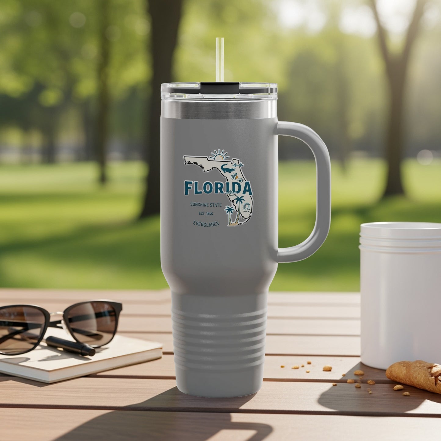 Grey tumbler with Florida map graphic and handle, outdoors on a table.
