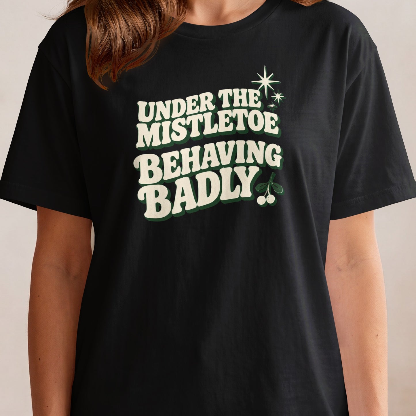 Black t-shirt with "UNDER THE MISTLETOE BEHAVING BADLY" text and mistletoe graphic.