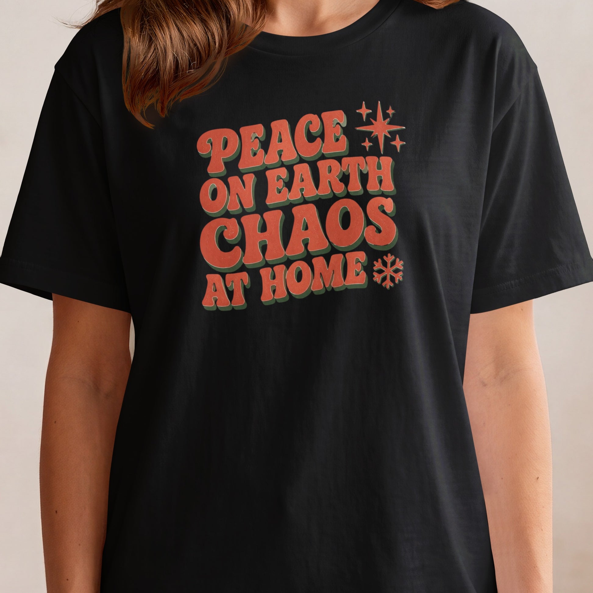 Black t-shirt with red and green text "PEACE ON EARTH CHAOS AT HOME".