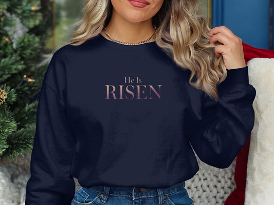 Navy sweatshirt with "He is Risen" text in gradient pink and purple.