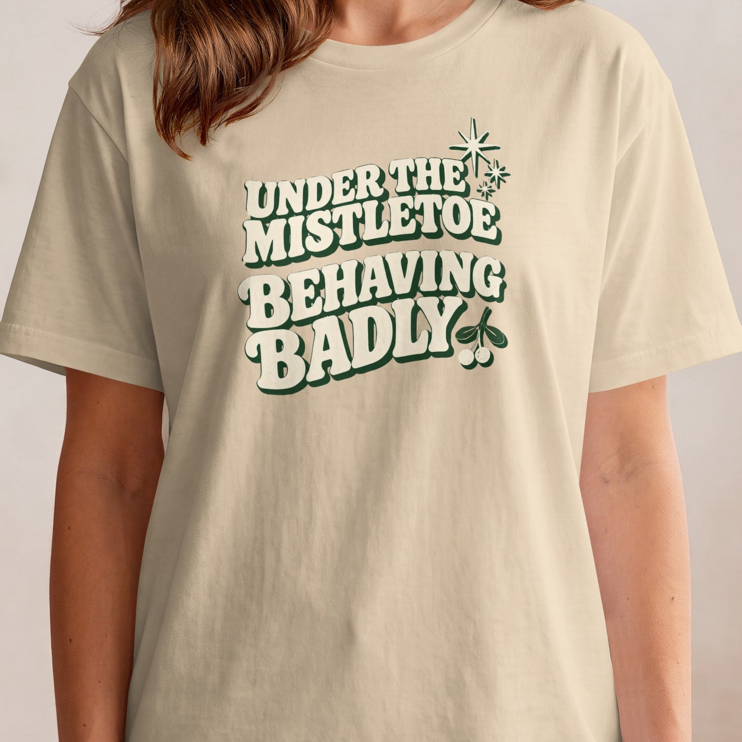 Cream t-shirt with "Under the mistletoe behaving badly" text and mistletoe graphic.