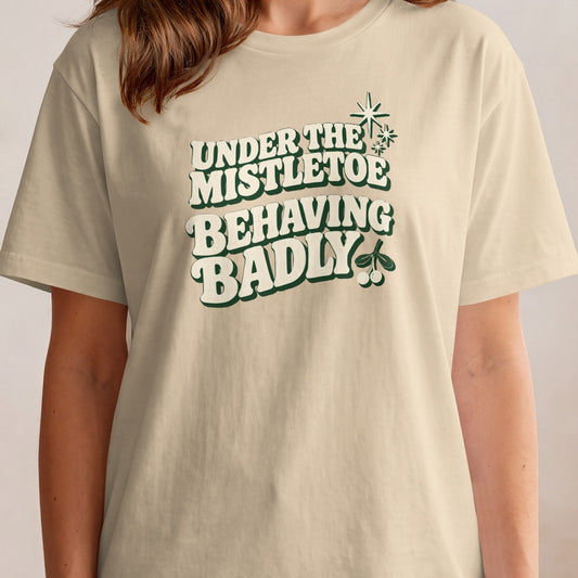 Cream t-shirt with "Under the mistletoe behaving badly" text and mistletoe graphic.