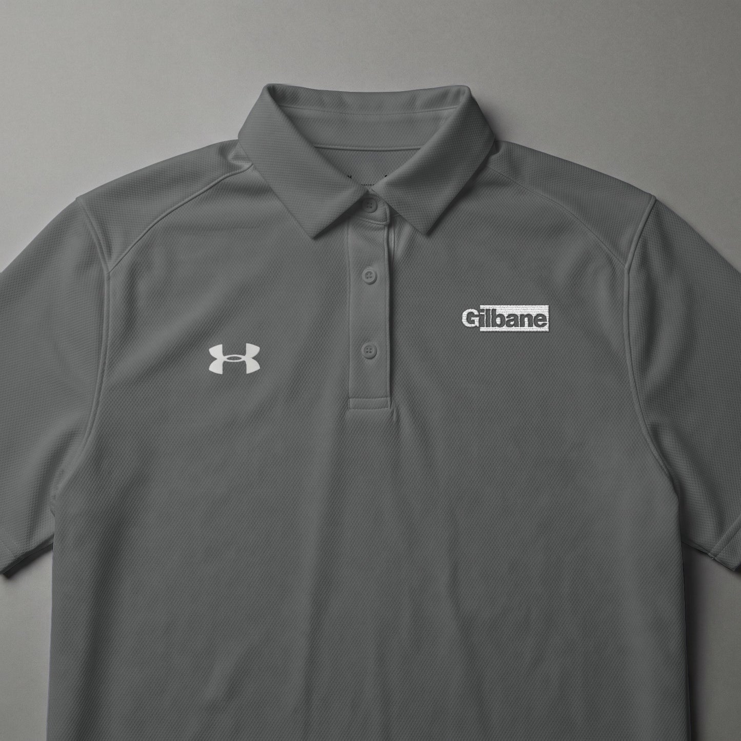 Gray Under Armour polo shirt with white Gilbane logo.