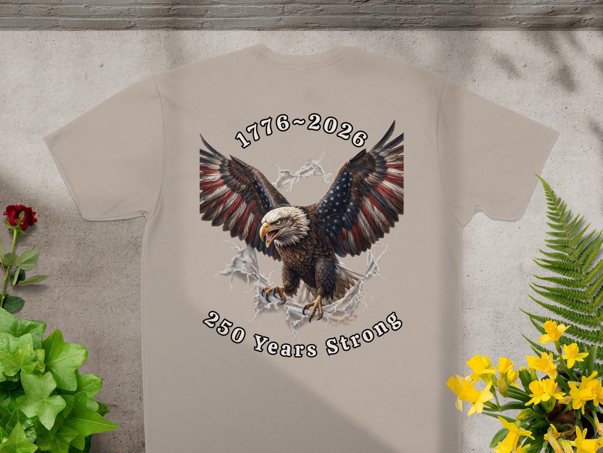Tan t-shirt featuring an eagle breaking through a torn flag with "1776-2026 250 Years Strong" text.