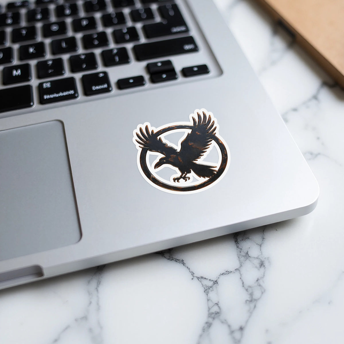 Black silhouette of a bird of prey within a circular emblem on a laptop.