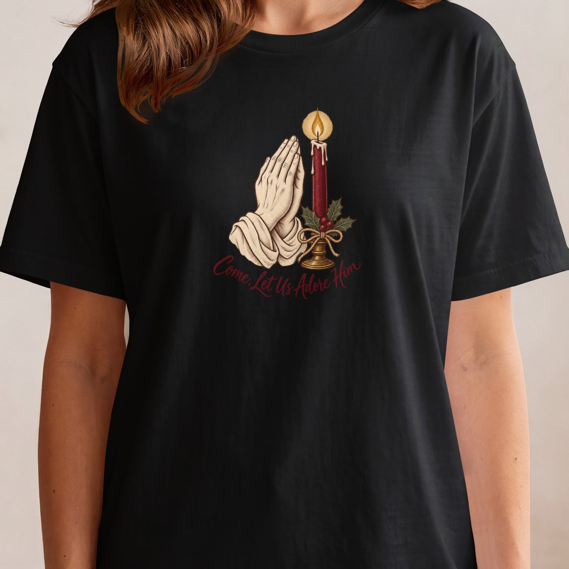 Black t-shirt with praying hands, candle, holly, and text "Come, Let Us Adore Him".