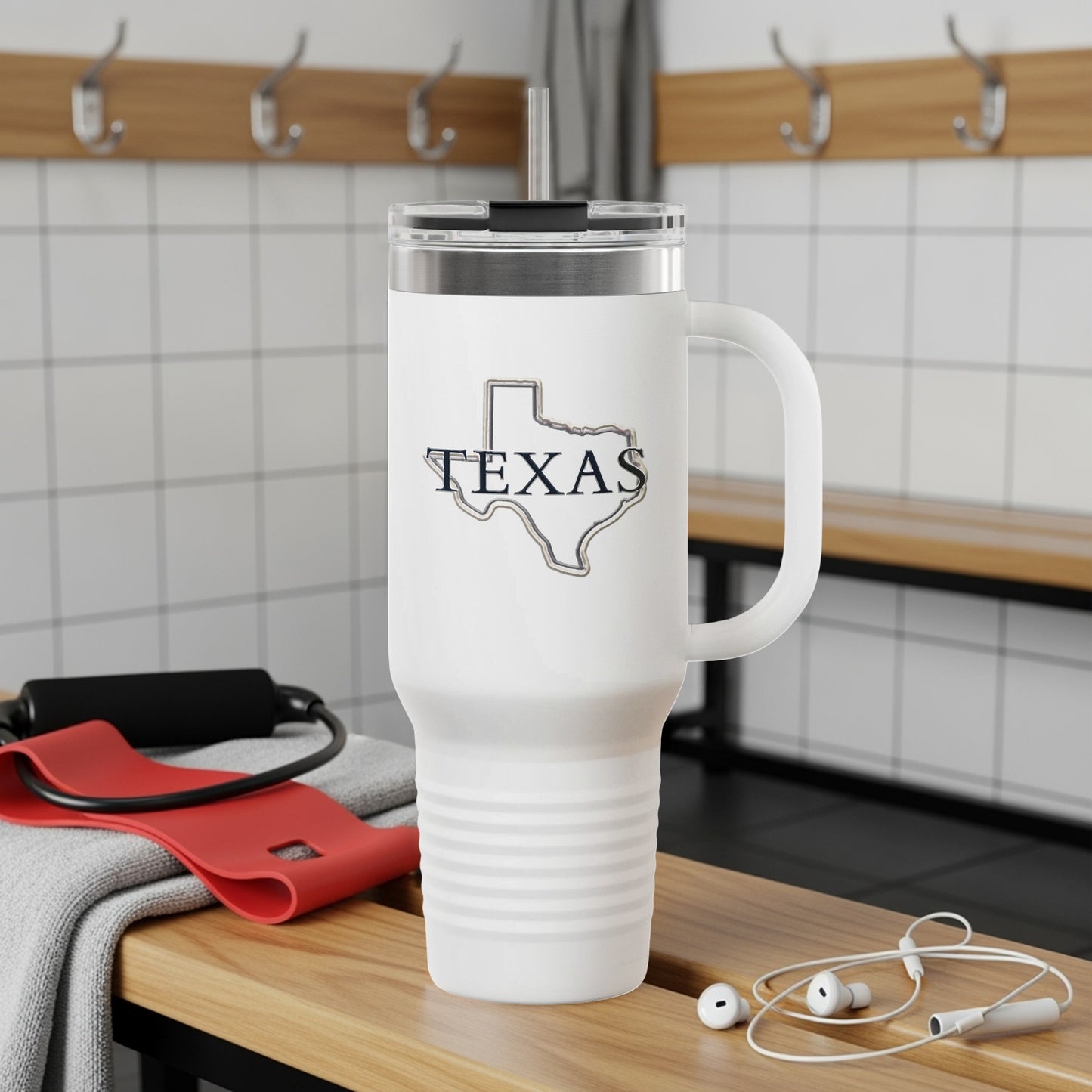 White tumbler with "TEXAS" in outline on a gym bench with headphones and resistance band.