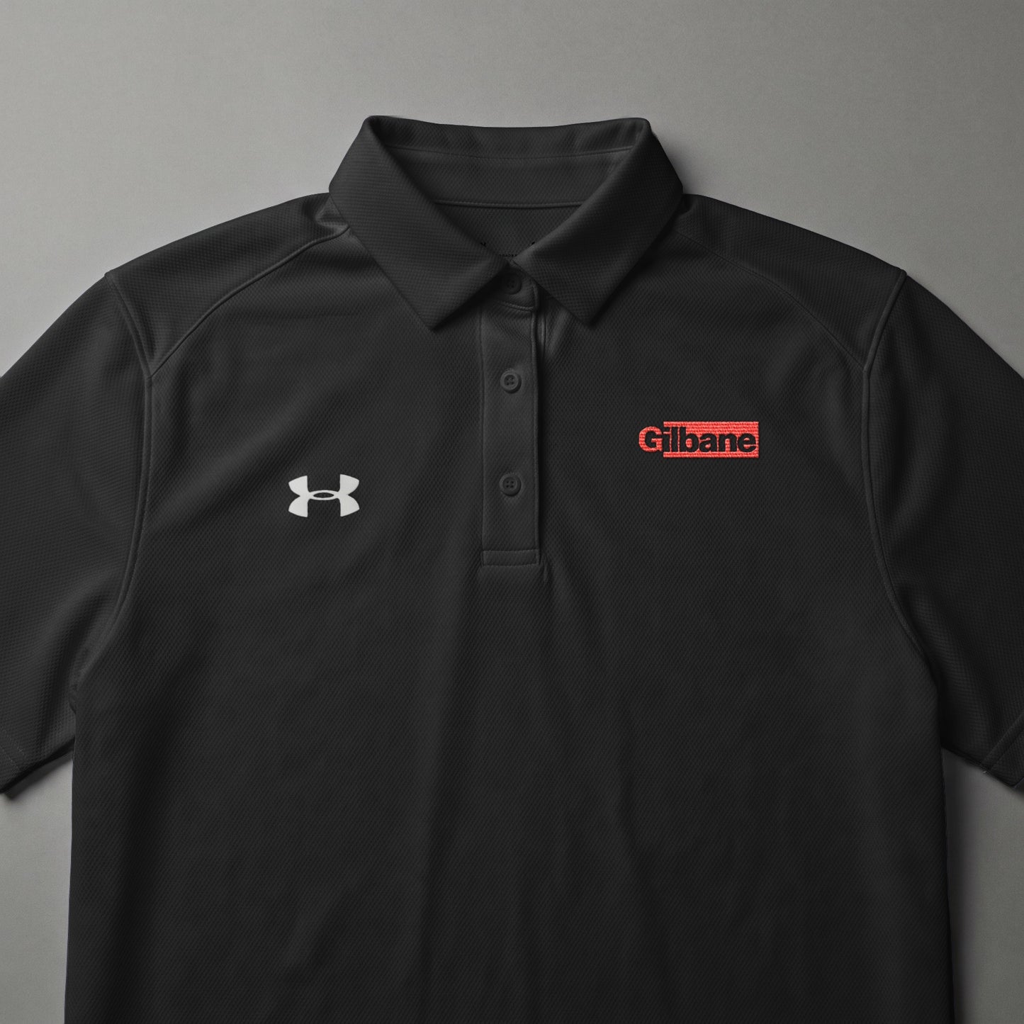 Black Under Armour polo shirt with red Gilbane logo on chest.