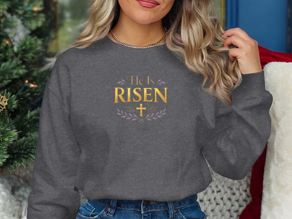 Dark gray crewneck sweatshirt with gold "He Is Risen" text and a cross.