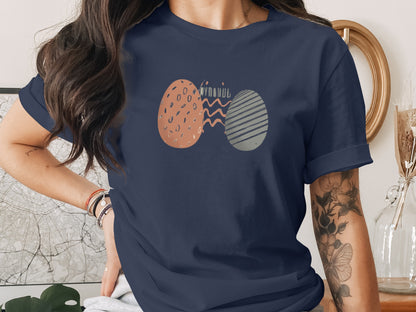 Stylish Abstract Eggs Wavy Lines Graphic Navy Blue product type
Navy blue shirt
Abstract design
Egg graphic
Speckled pattern
Striped pattern
Wavy lines
Graphic print
Casual top
Short sleeve
Round neck tee
Modern design
Unique print
Easter eggs
Spring fashion
Art tee
Unisex apparel
Graphic tee
Clothing
Fashion top
Designer print
