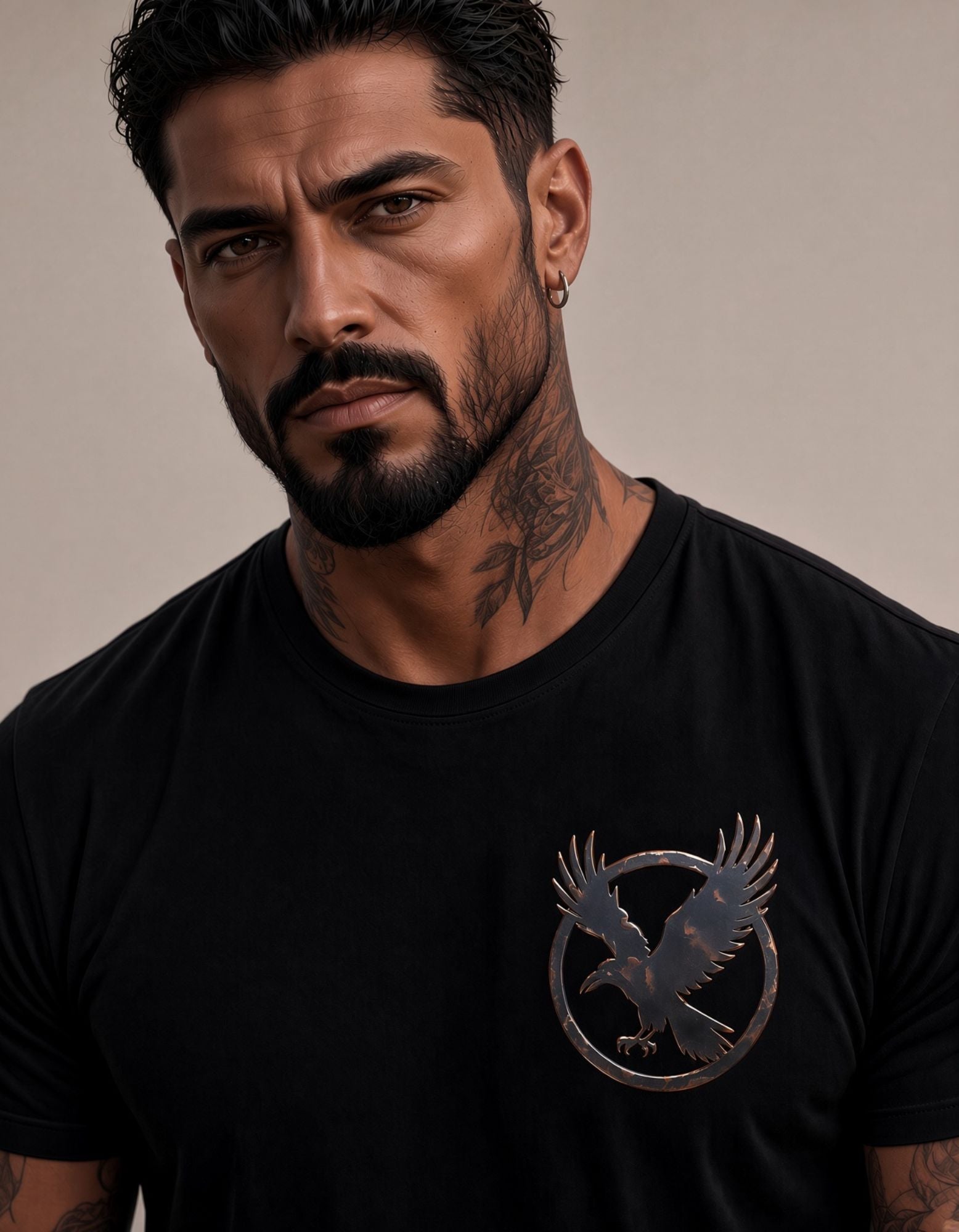 A close-up of a man wearing a black crew-neck t-shirt with a metallic bronze raven graphic on the left chest, set against a neutral beige background.