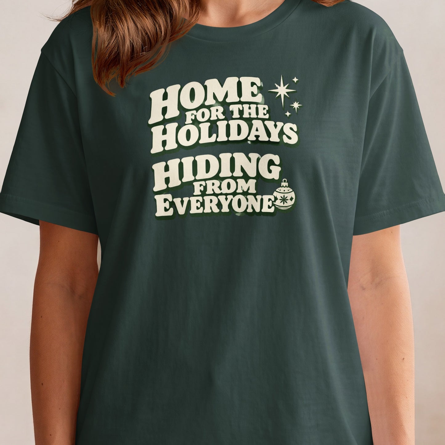 Dark green t-shirt with white text "HOME FOR THE HOLIDAYS HIDING FROM EVERYONE".