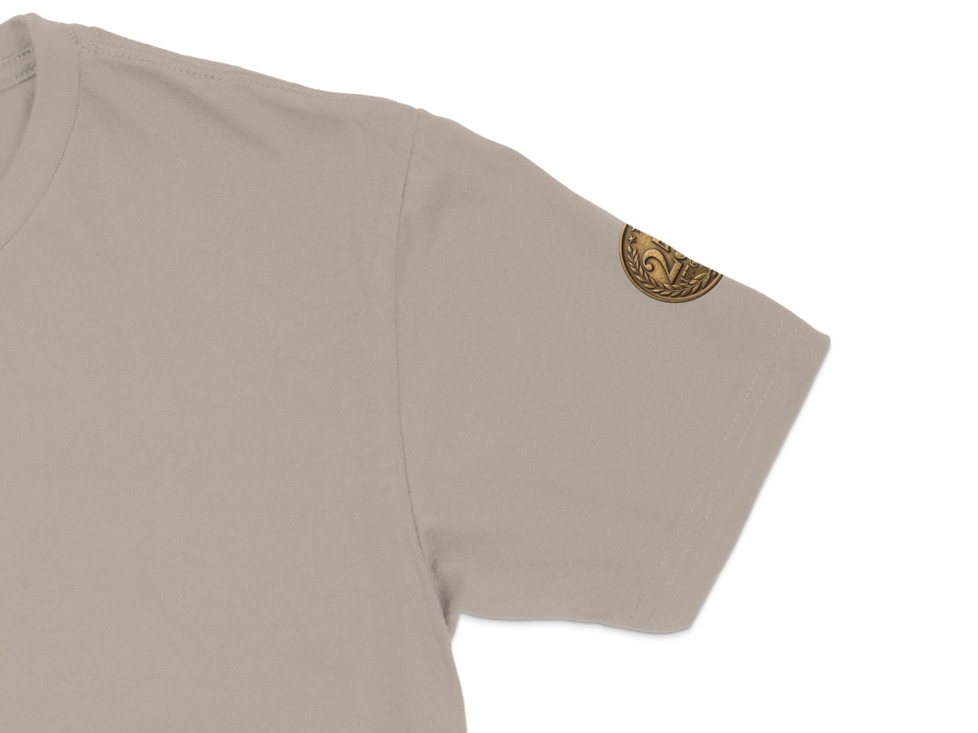 Beige t-shirt sleeve with small circular embroidered emblem on the bicep.