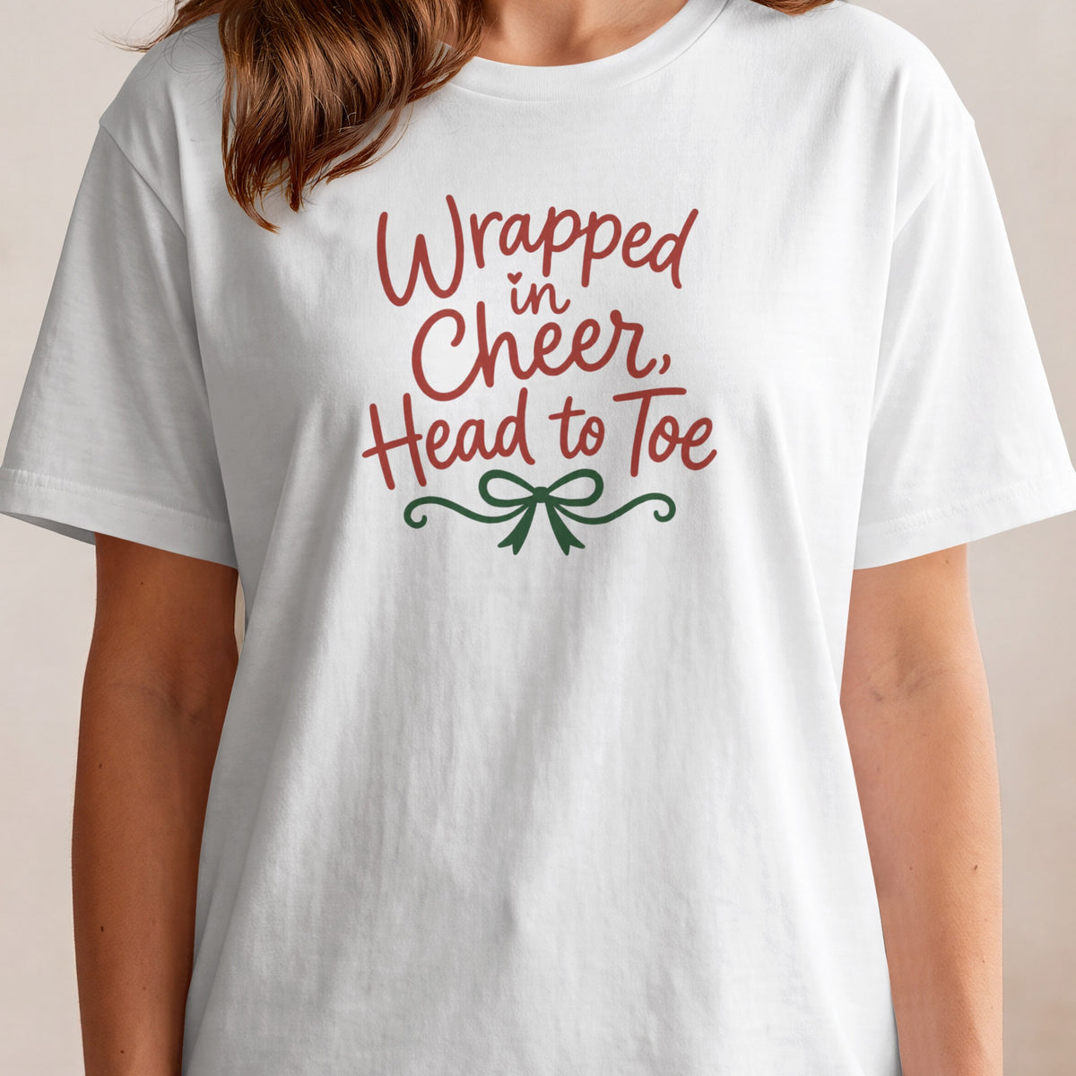 White t-shirt with red text "Wrapped in Cheer, Head to Toe" and green bow graphic.