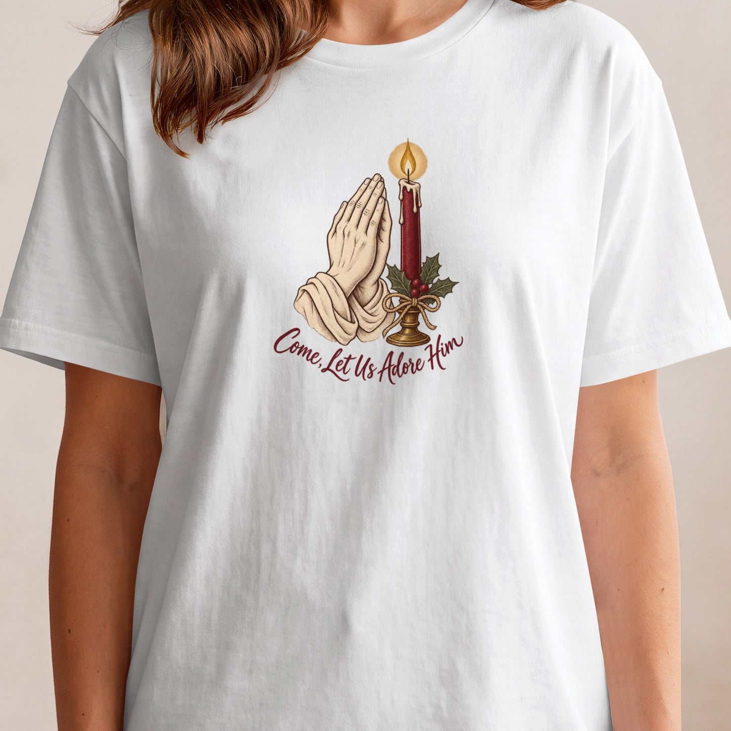 White t-shirt with praying hands, candle, holly, and text "Come, Let Us Adore Him."