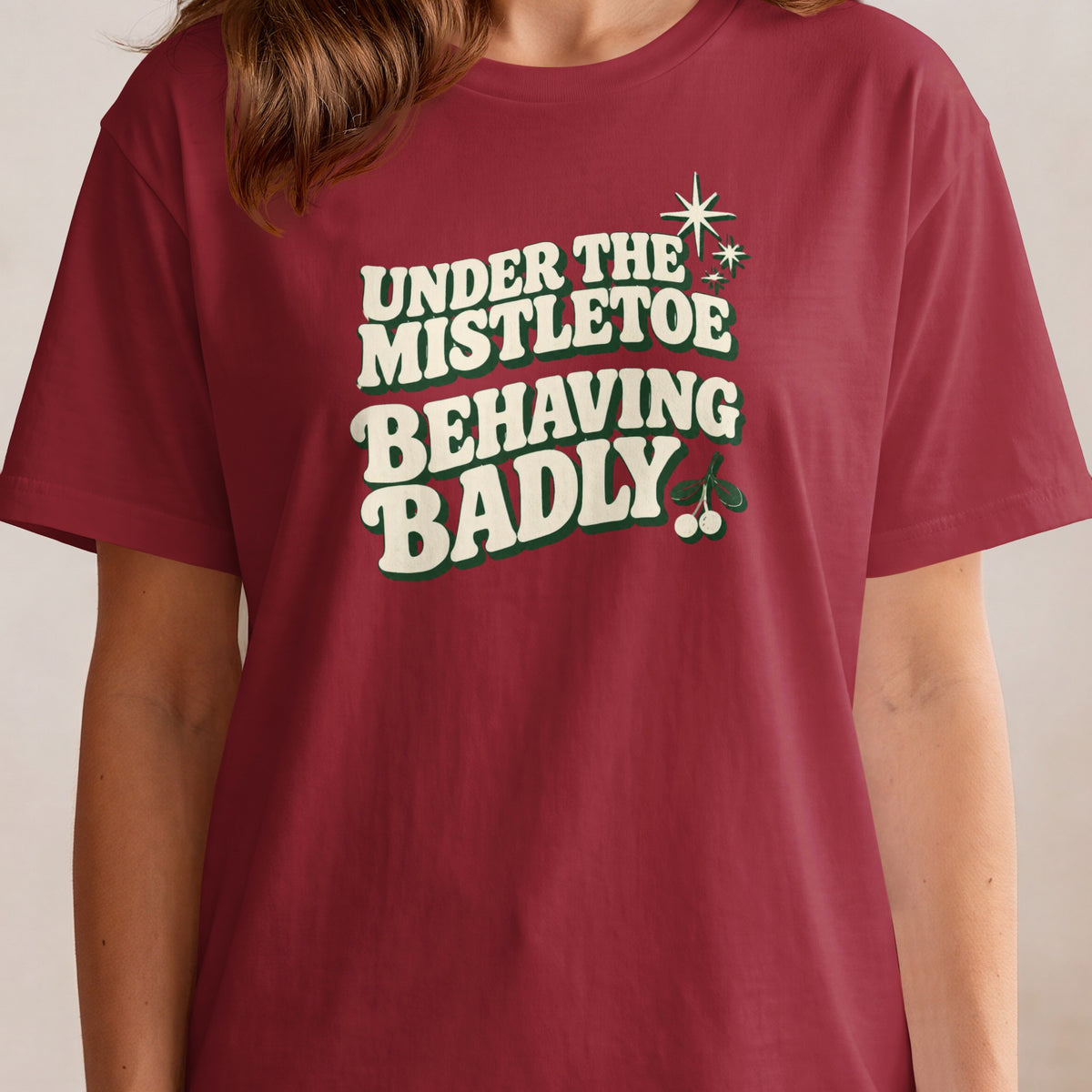 Maroon t-shirt with "UNDER THE MISTLETOE BEHAVING BADLY" text and mistletoe graphics.