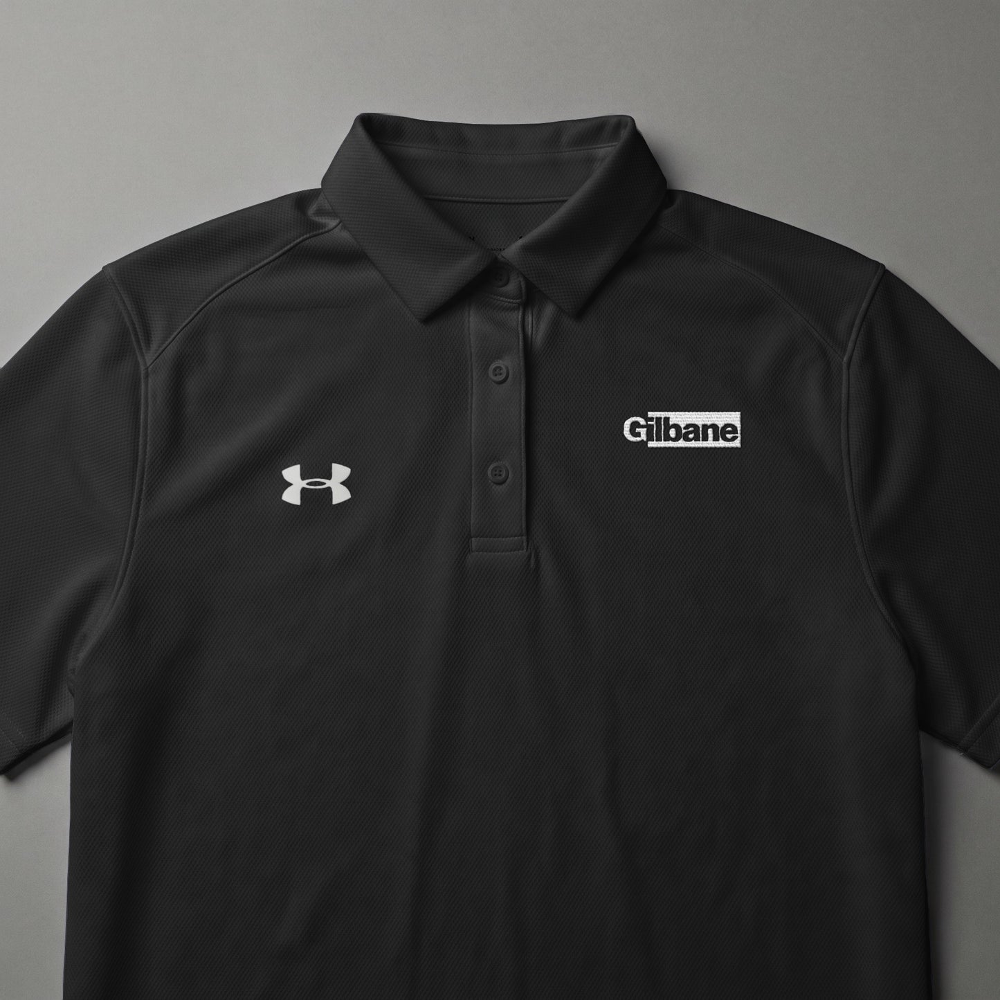 Black Under Armour polo shirt with Gilbane logo on chest.