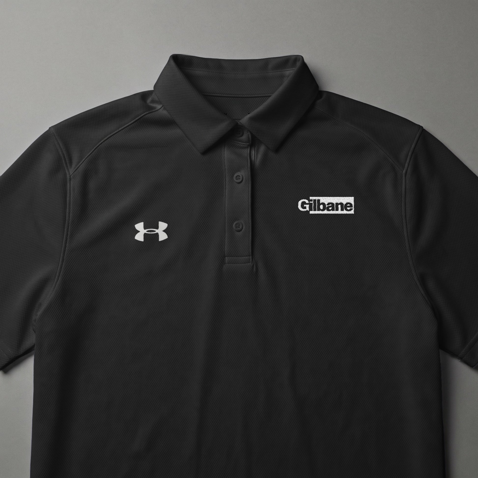 Black Under Armour polo shirt with Gilbane logo on chest.