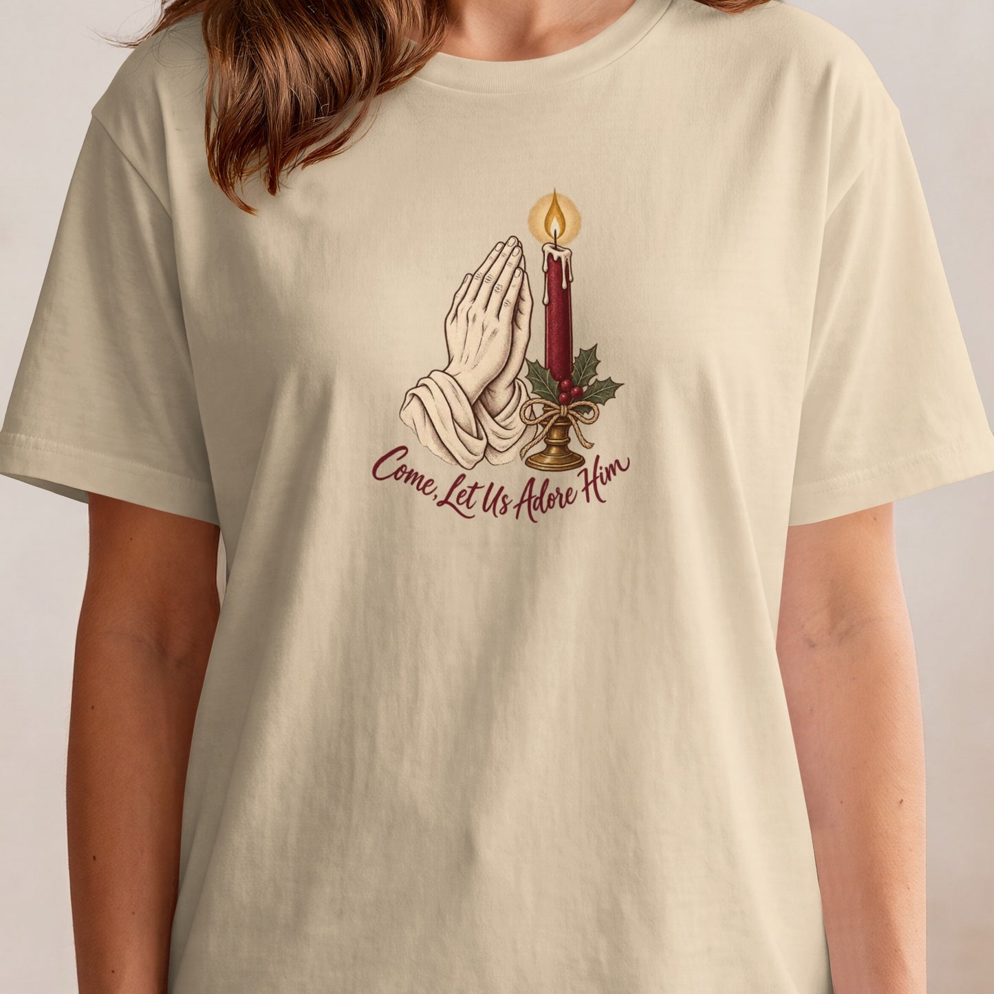 Cream t-shirt with praying hands, candle, holly, and text "Come, Let Us Adore Him".