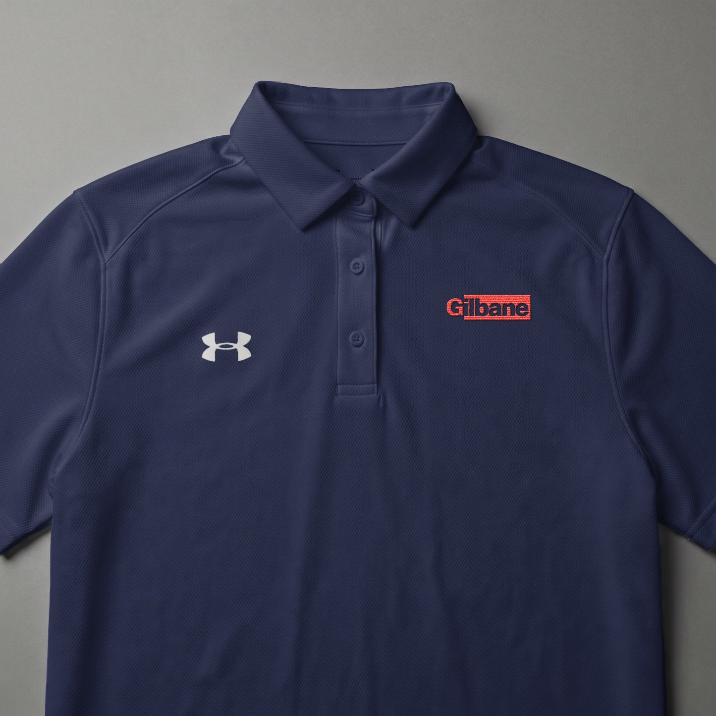 Navy blue Under Armour polo shirt with Gilbane logo on chest.