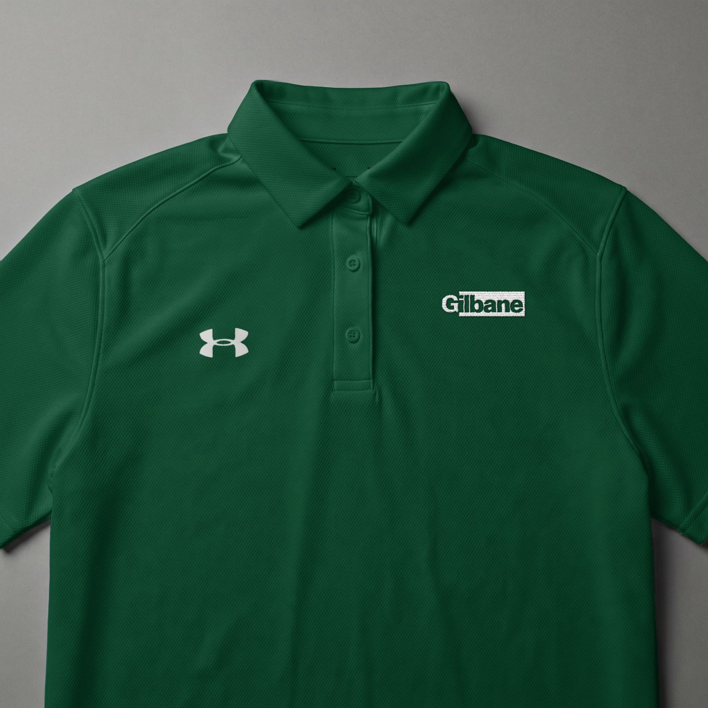 Green Under Armour polo shirt with white Gilbane logo on the chest.