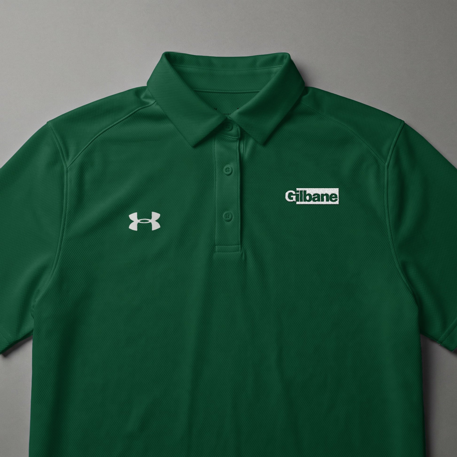 Green Under Armour polo shirt with white Gilbane logo on the chest.