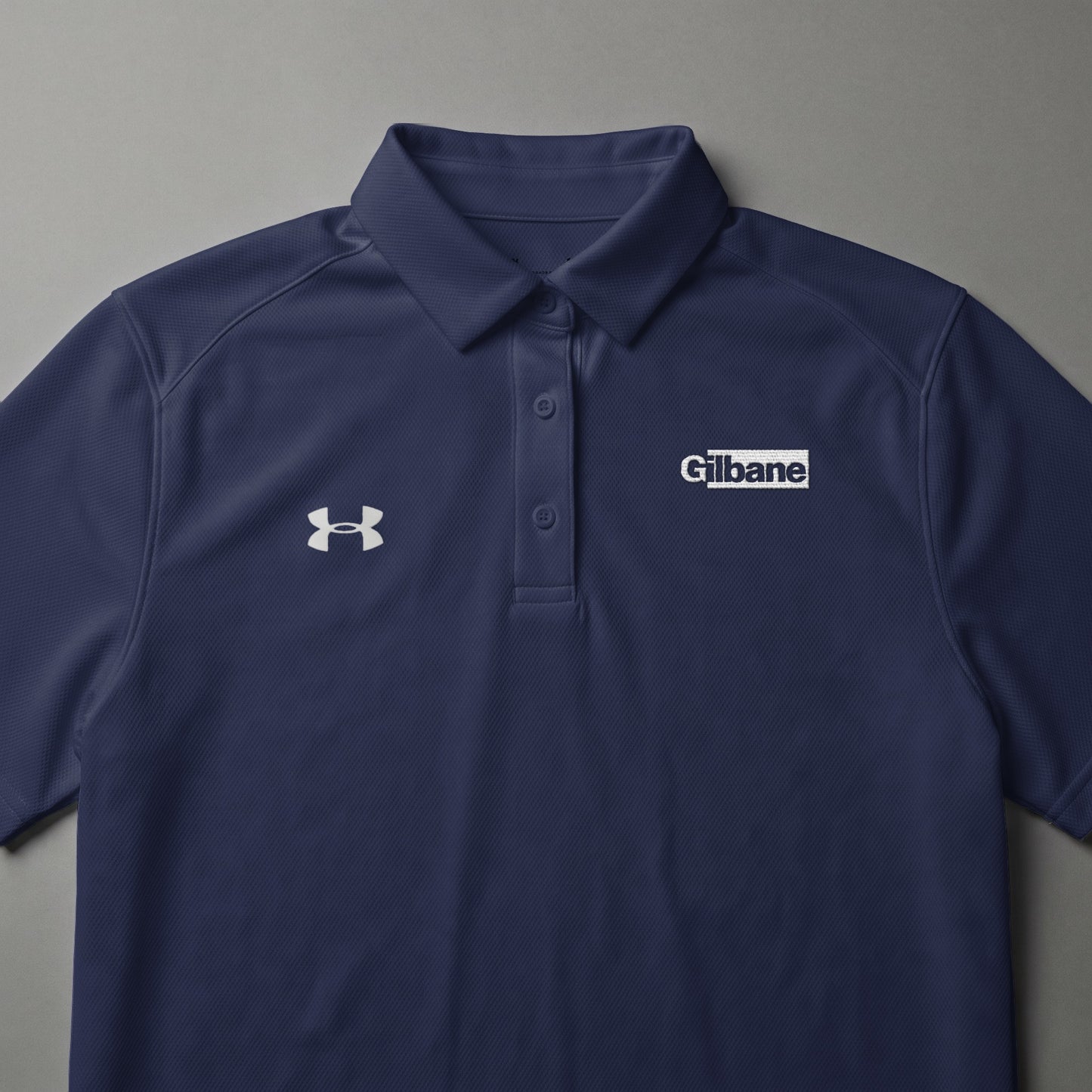 Navy blue Under Armour polo shirt with Gilbane logo on the chest.