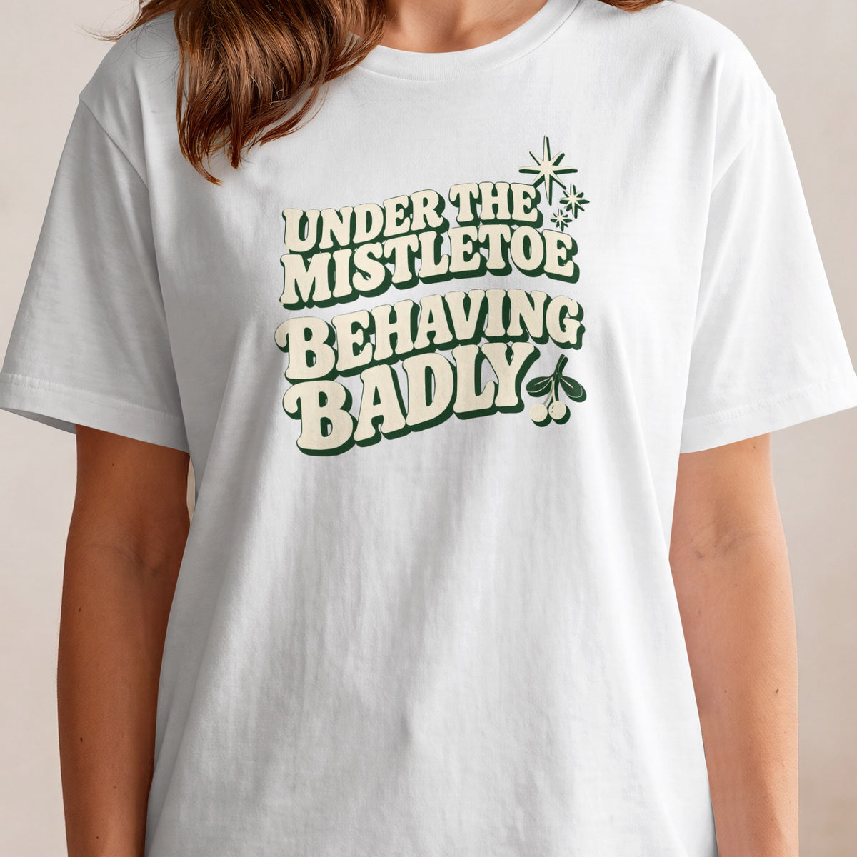 White t-shirt with "Under the Mistletoe Behaving Badly" text and mistletoe graphic.